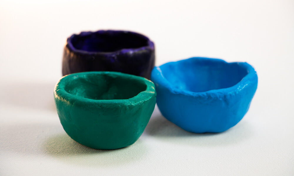 Three pinch pots made from air dry clay each painted with various colours green, blue and black.