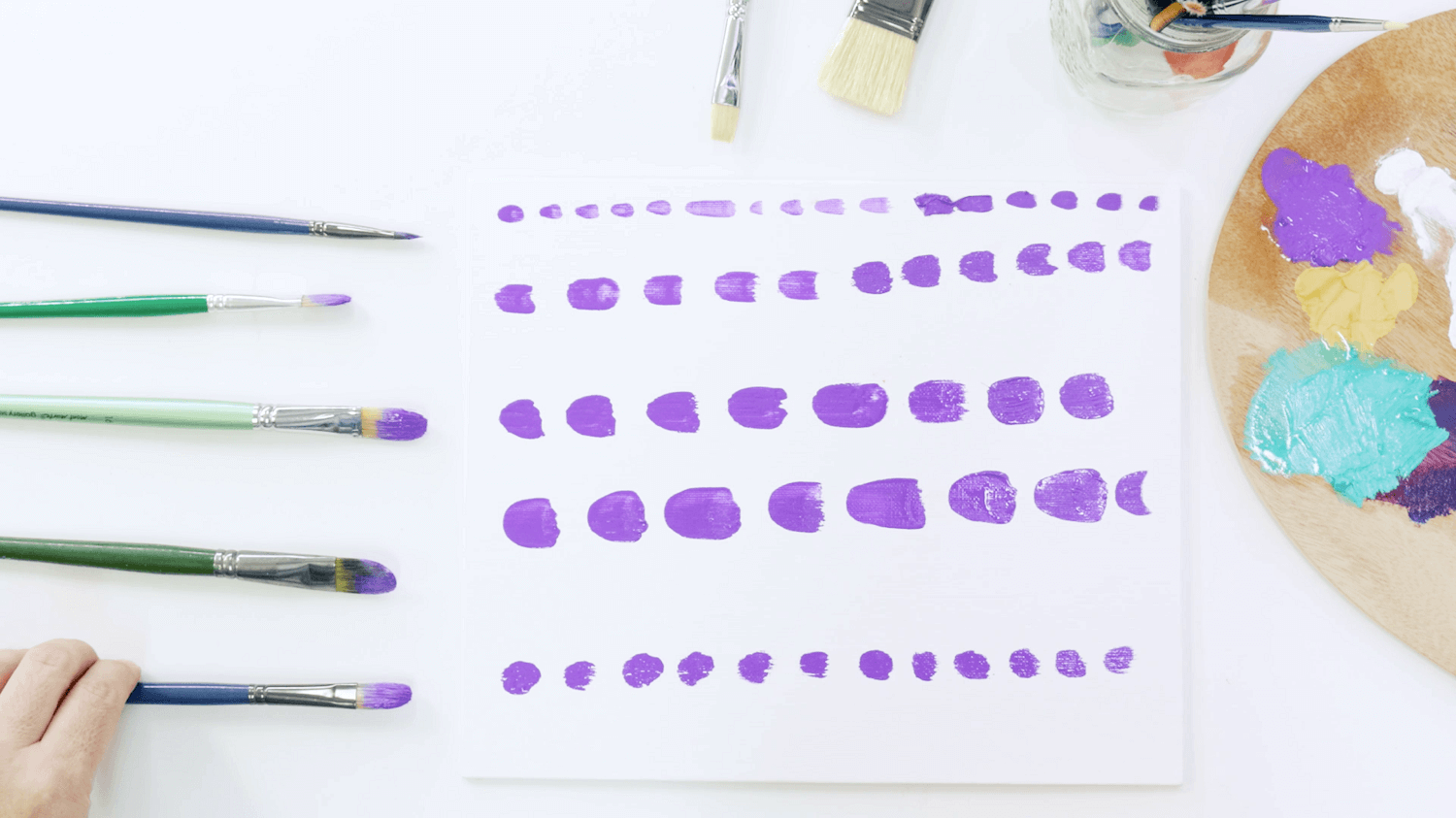 Filbert brushes lined up next to purple lines of paint using the various sizes of oil paint brush.