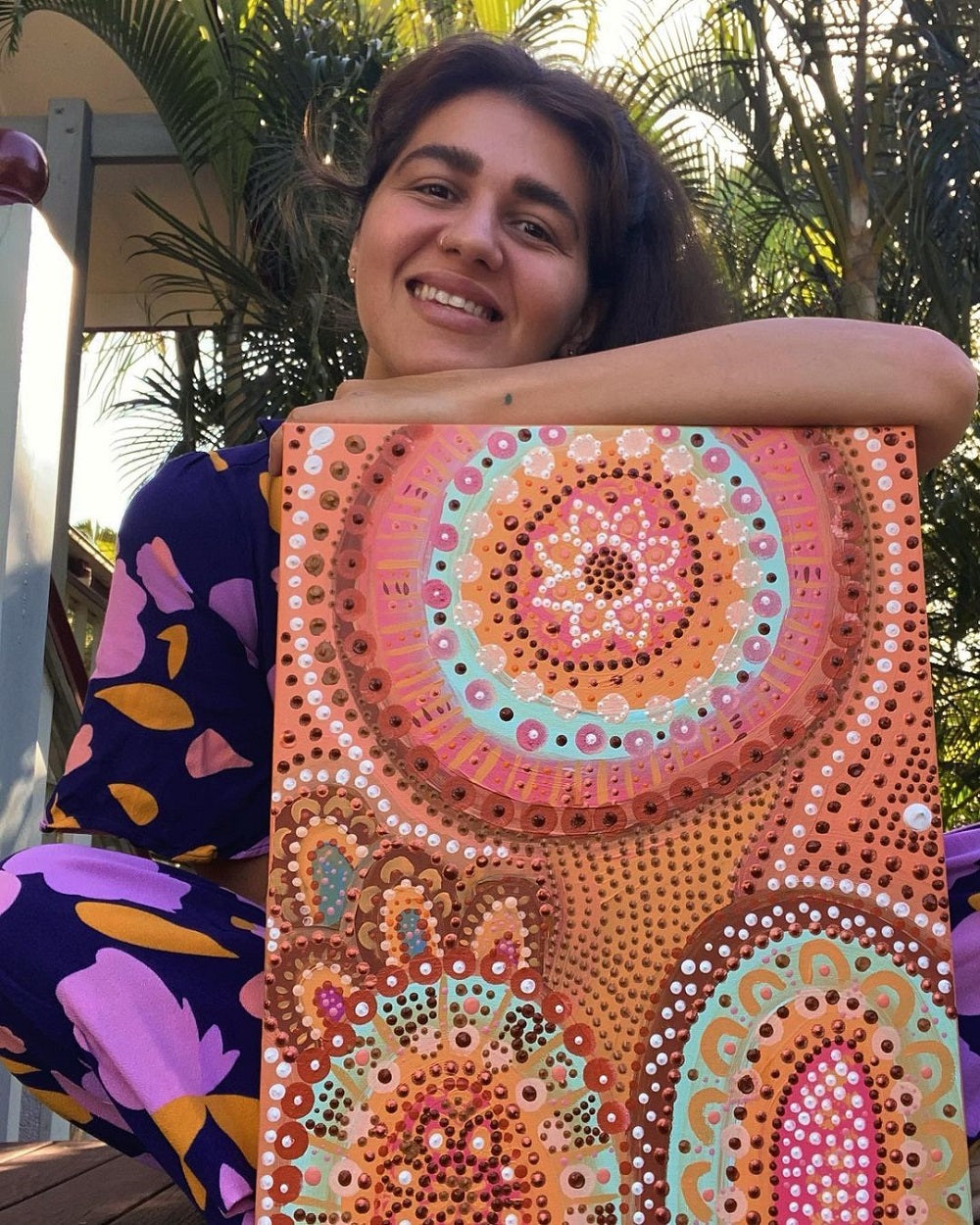 Jacinta holding her bright artwork of colourful dots on canvas.