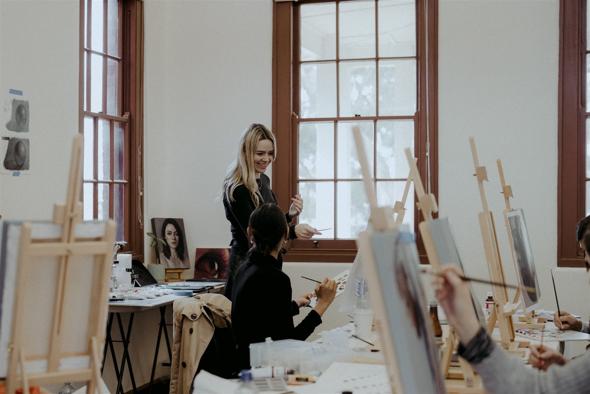 Rachelle in her workshop next to large windows and canvases teaching students.