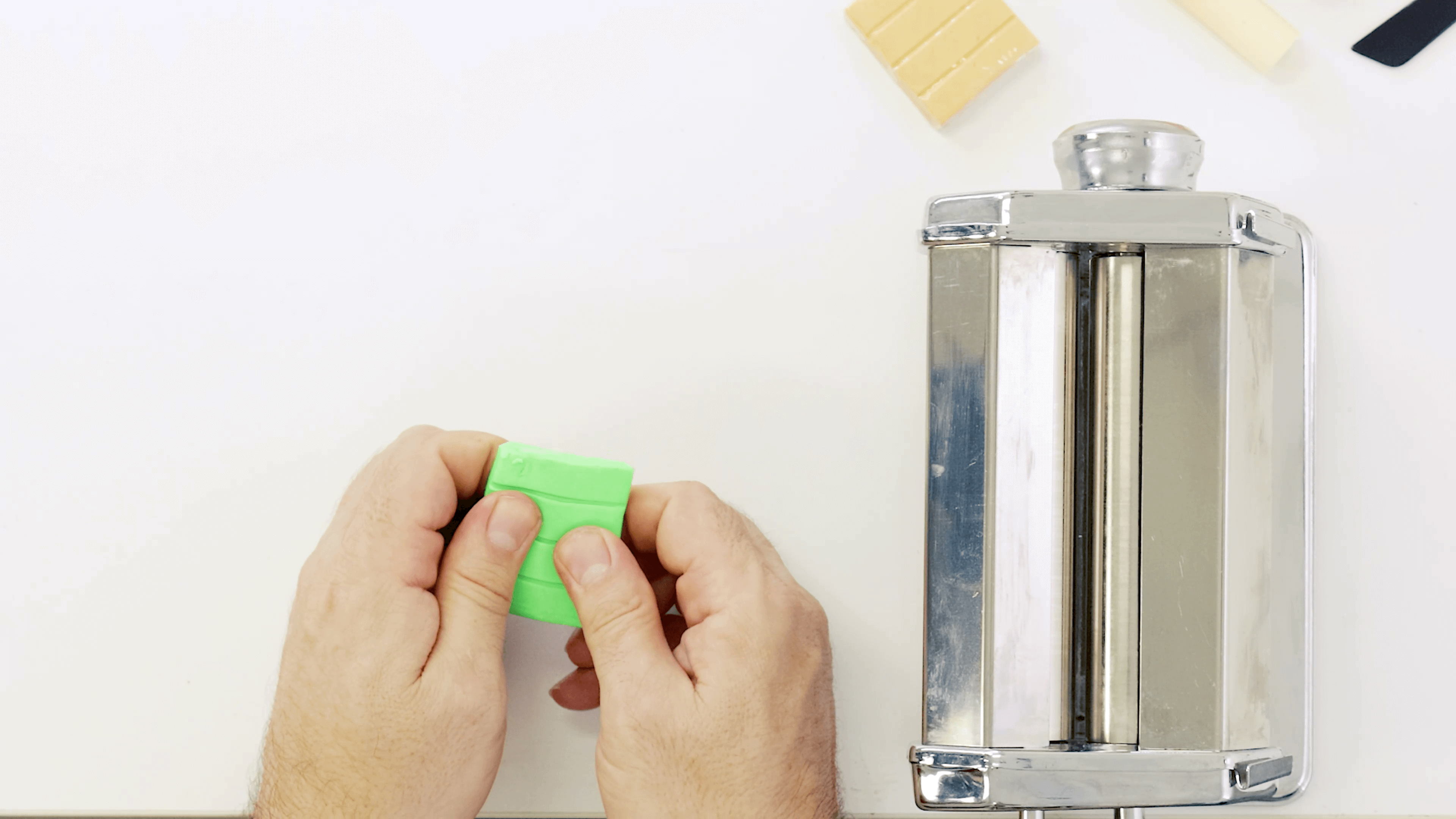 Hand holding a lime green slab of polymer clay to smooth it out before going into a clay press.