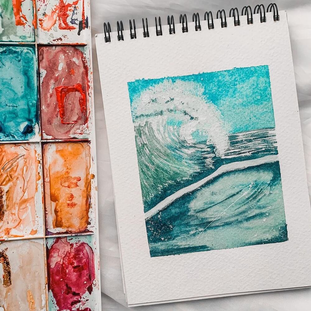 Watercolour painting of a wave break with watercolour pans next to it.