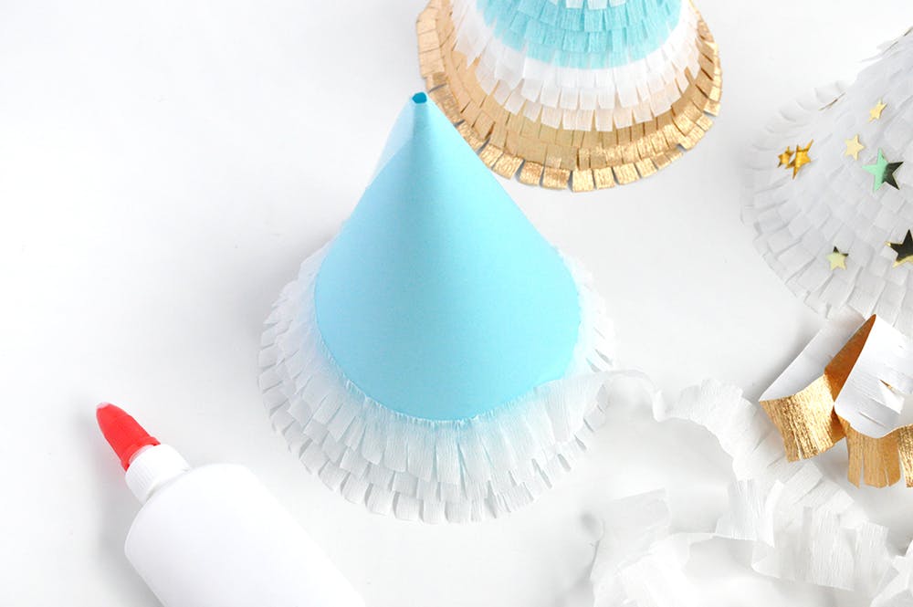 Light blue party hats on a table with craft glue next to it..