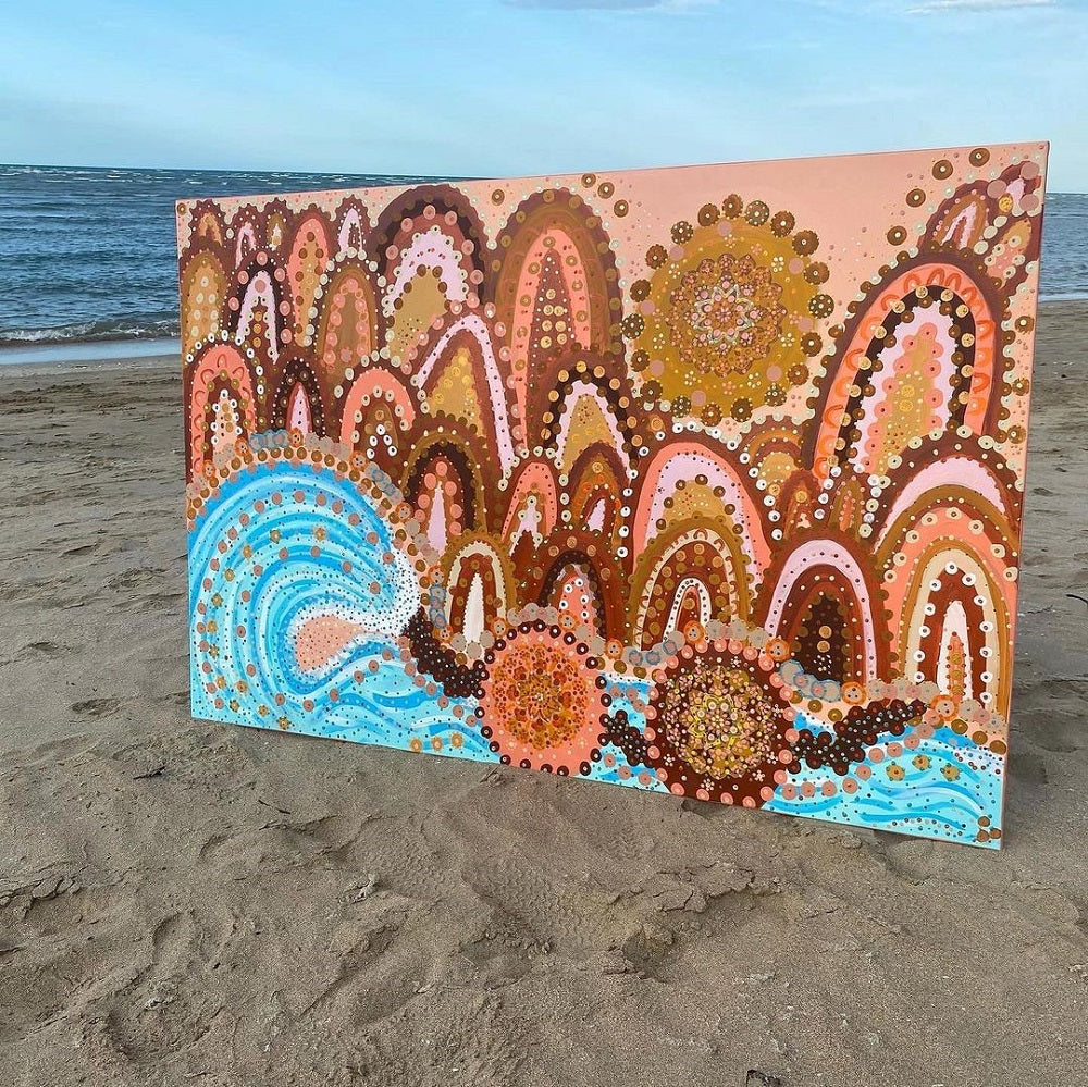 A bright contemporary Indigenous artwork on canvas standing on the beach.