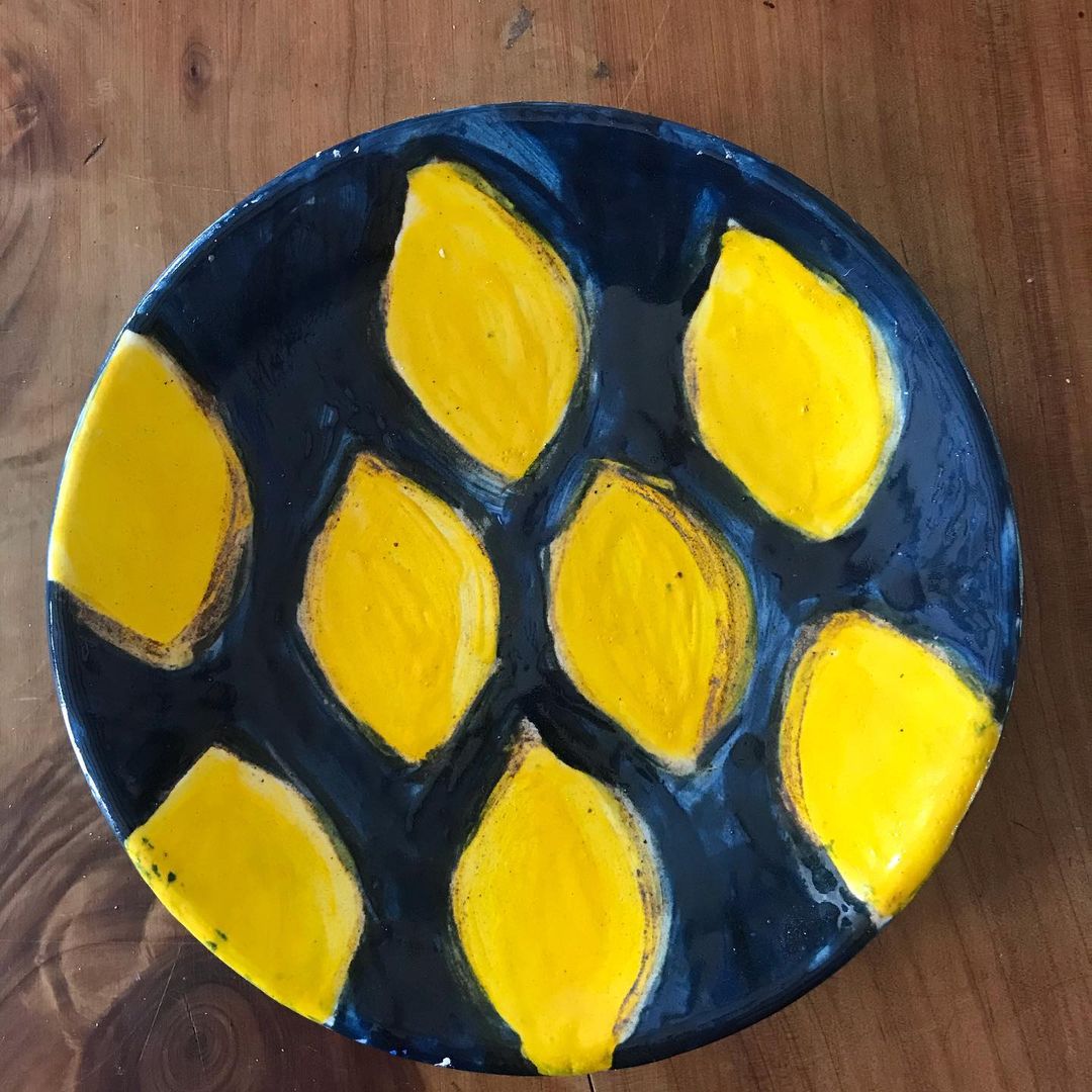 A glazed dark blue plate with bright yellow lemons painted on top.