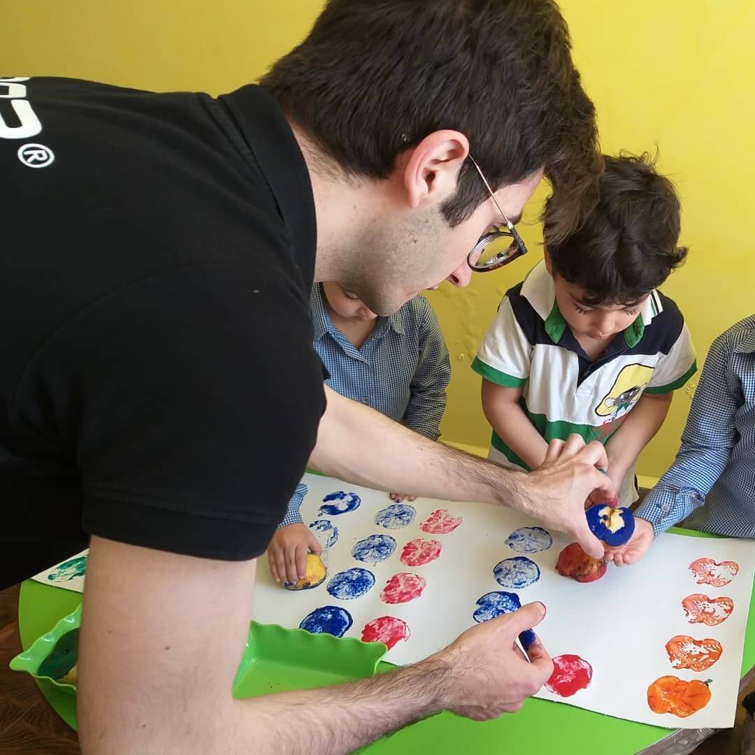 Ahmad Akrum and child using an apple to create coloured stamps with paint on paper.