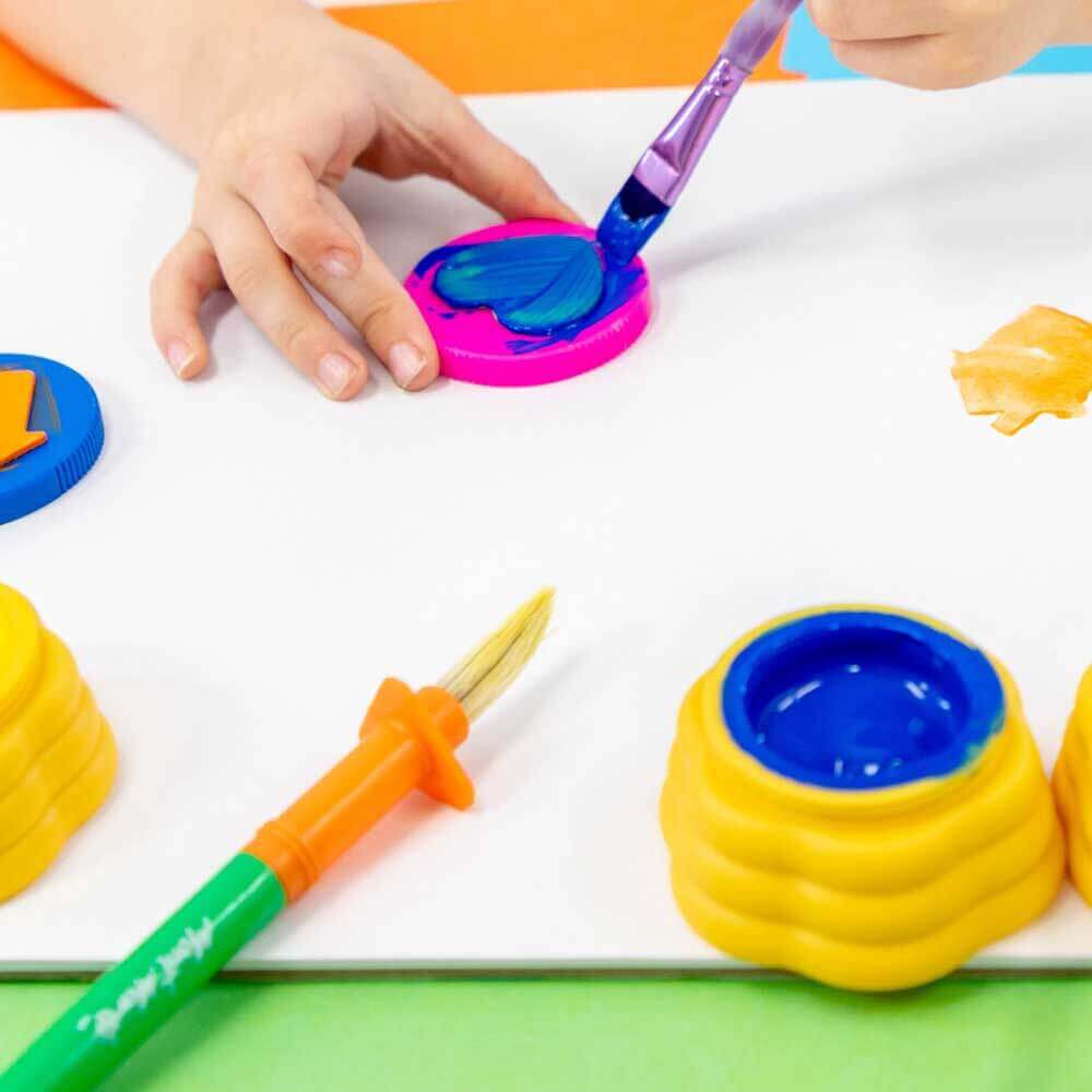 Hand holding a paint brush and painting a stamp to press on a child's artwork.