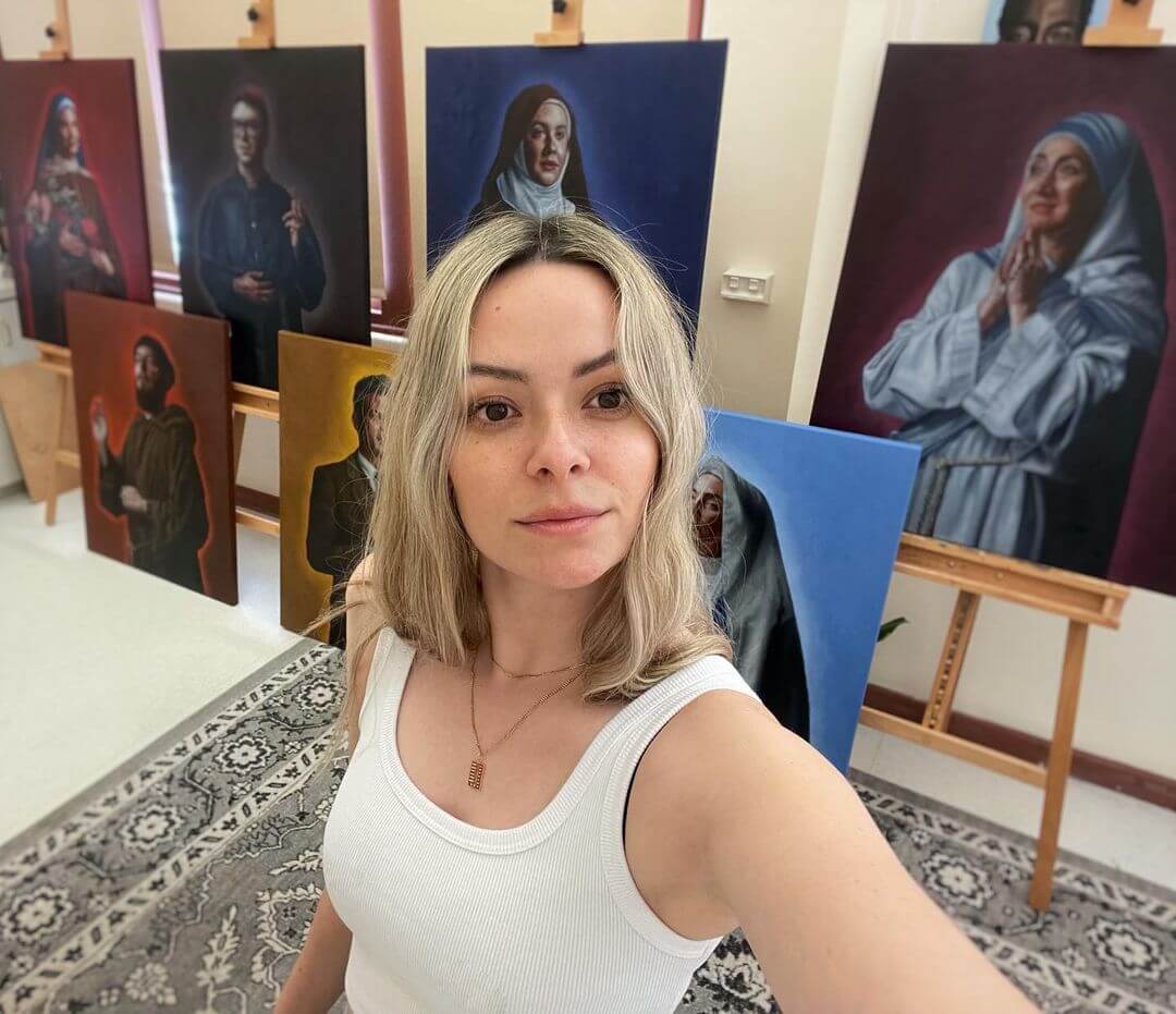 Rachelle holding the camera showing herself and 8 life sized Catholic saint oil paintings in the background.