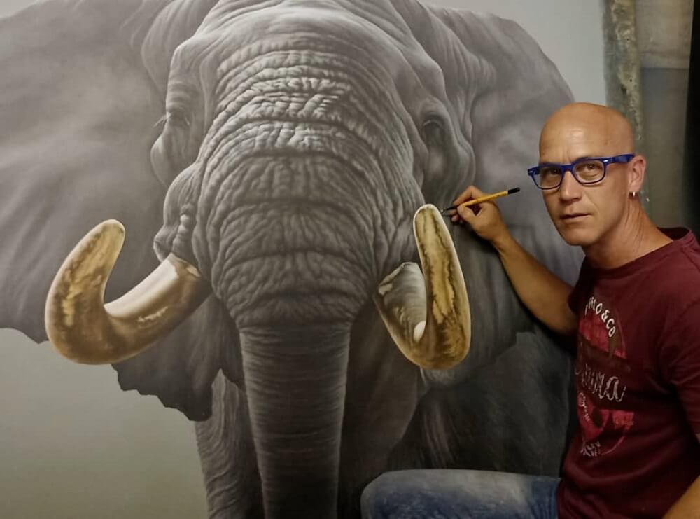 Dawie Mocke looking at the camera while painting a realistic elephant.