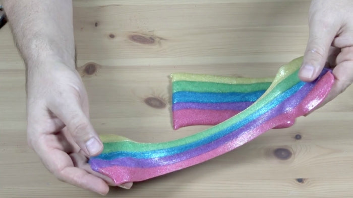Hand holding rainbow slime out on a wooden table.