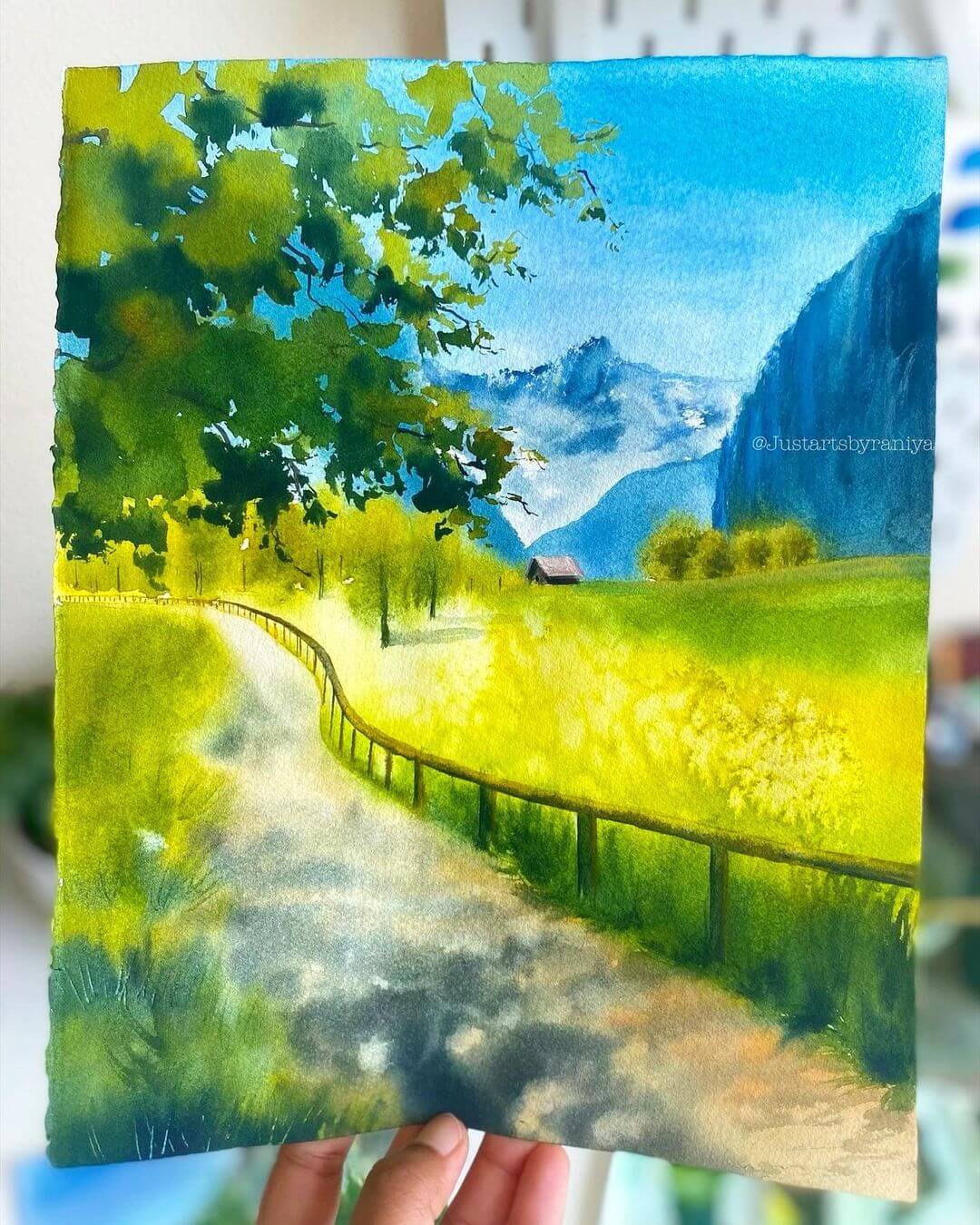 A green meadow water colour painting with mountains and a small house in the background.