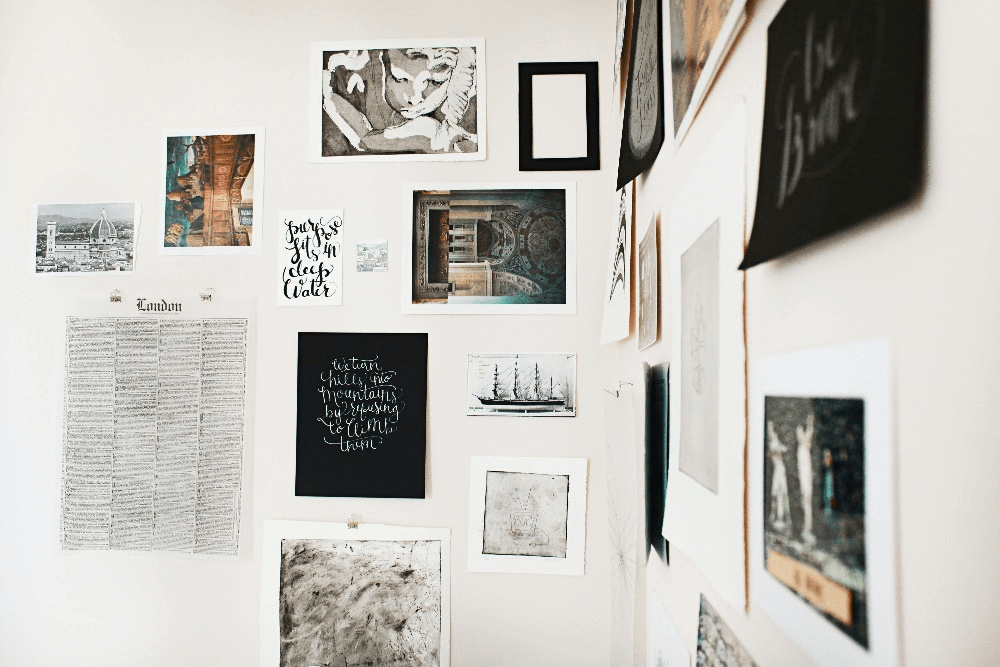 A white wall with various artworks of greyscale and colour hanging on the wall.