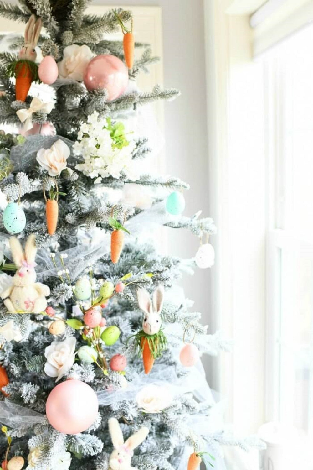 An Easter Christmas Tree with Easter decorations, a white tulle trim with carrots, rabbit ornaments and pastel baubles hanging off of the tree.