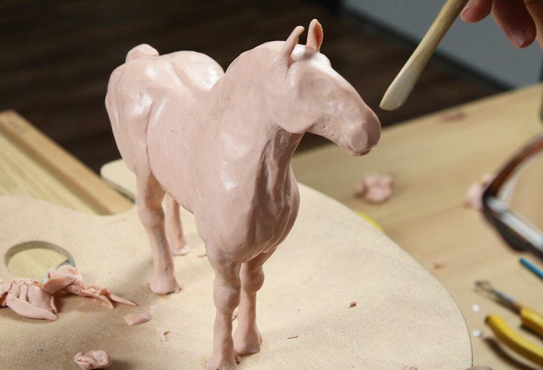 Horse sculpture being smoothed out with a clay tool.