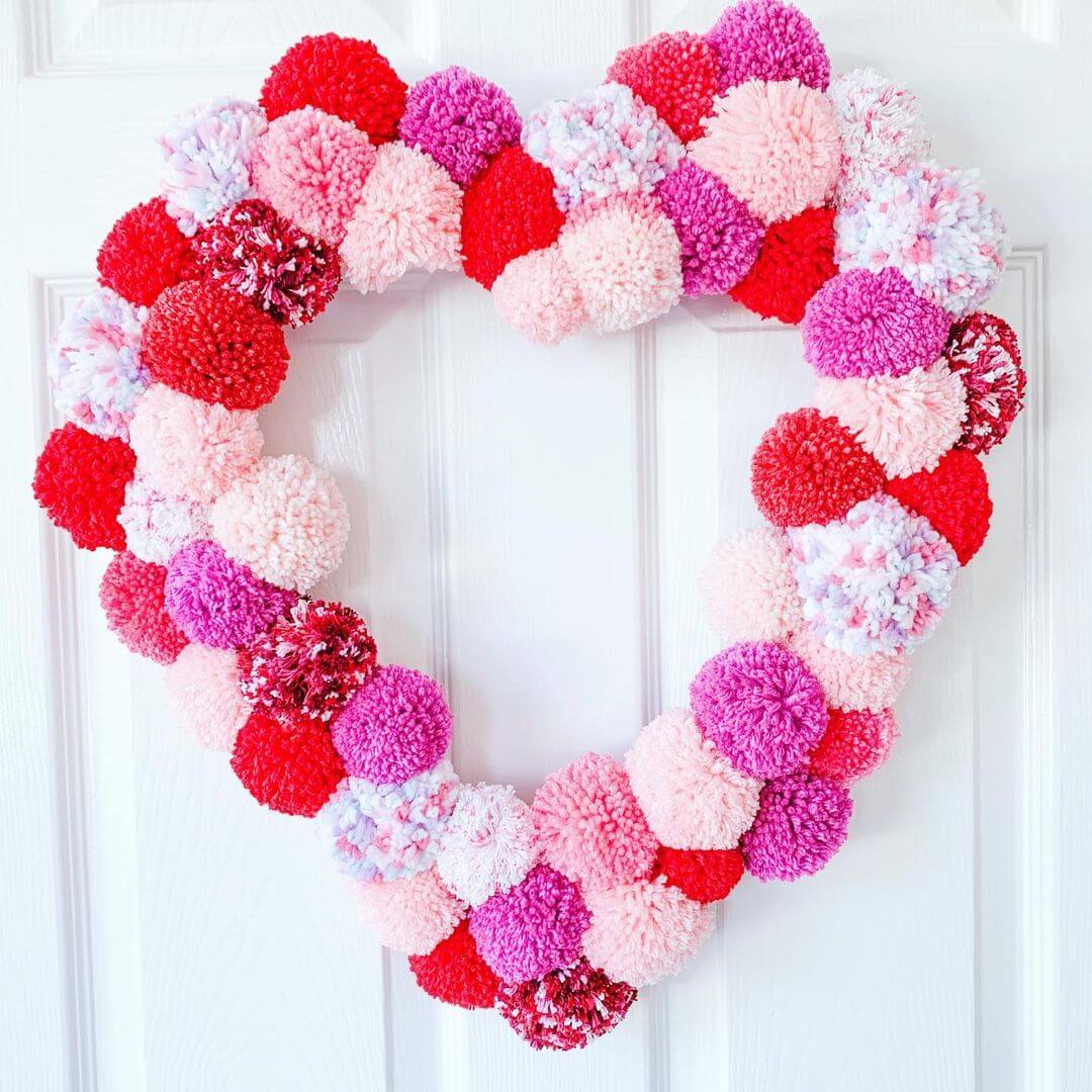 A coloured heart wreath with various pom poms decorated on it.