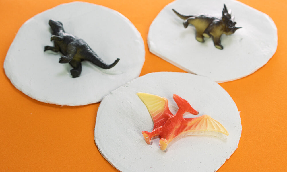 Three circular pans of air dry clay with three plastic dinosaur toys on top to create a fossil.