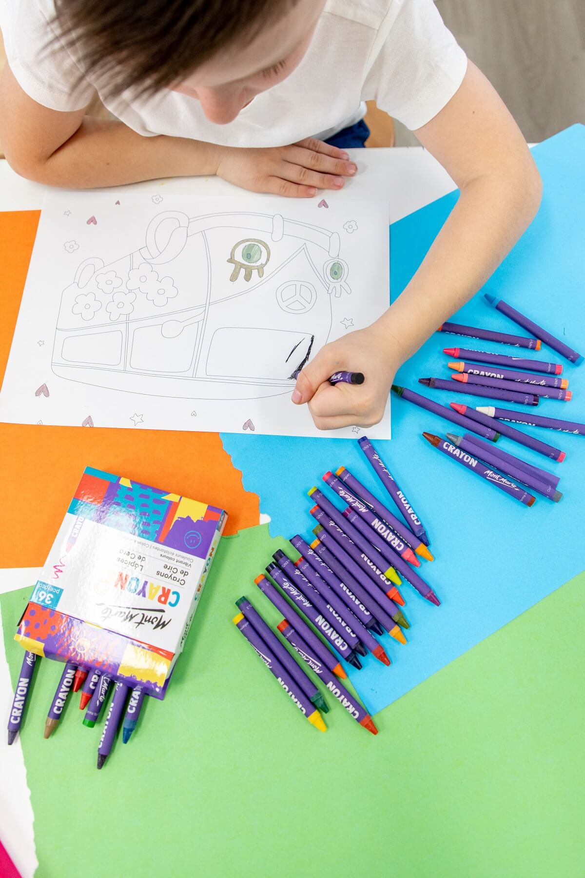 A child colouring in a car drawing with Mont Marte crayons on a coloured table.