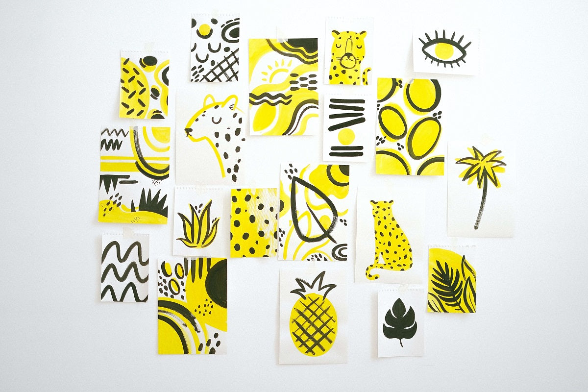 White wall with abstract yellow and black leopards, eyes, palm trees and shapes hanging on the wall.