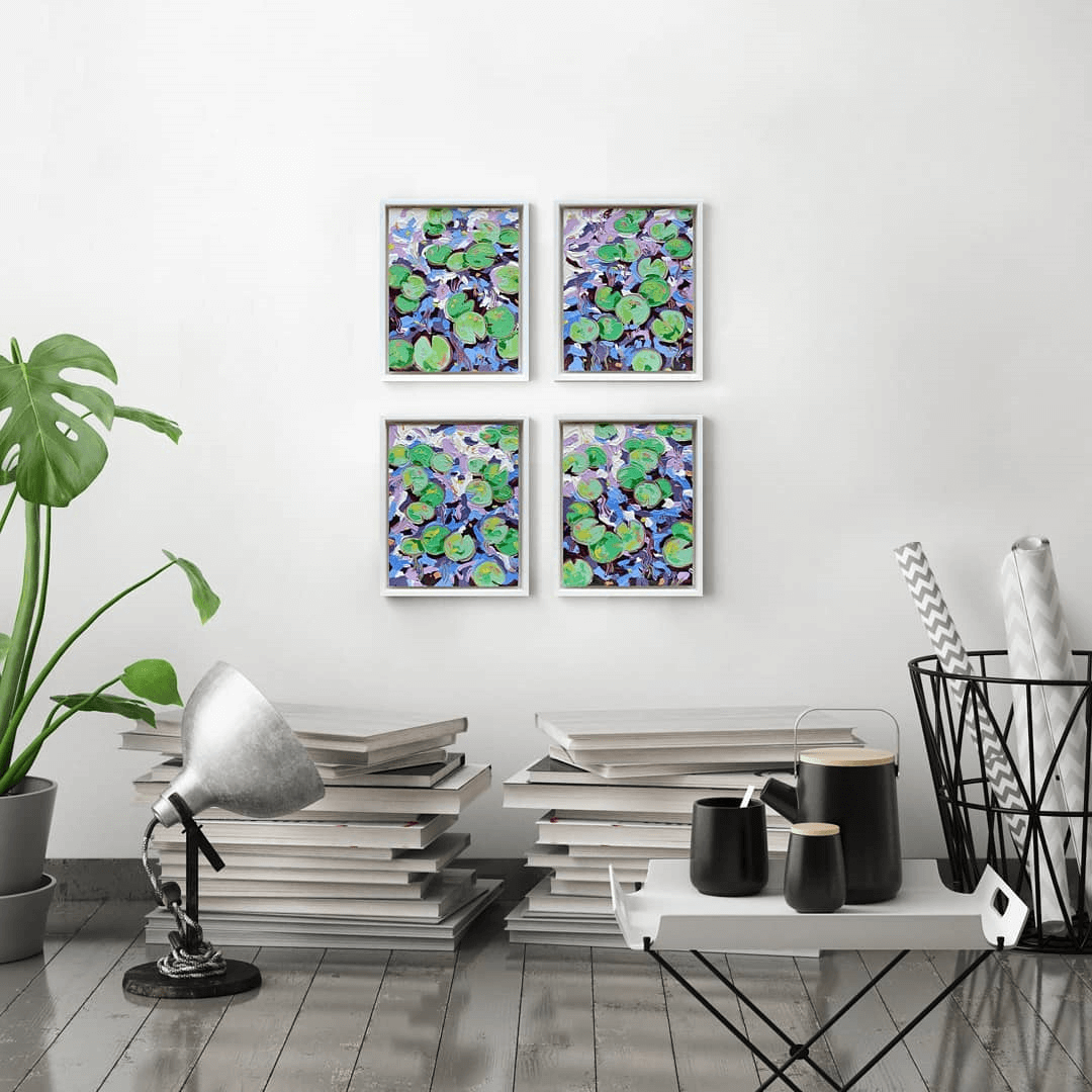 Four small lily pad paintings hanging on a white wall with books stacked close by.