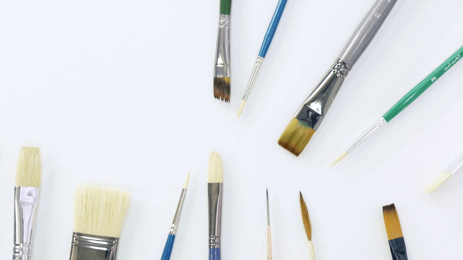 A range of different oil paint brush types laying flat on a white table.