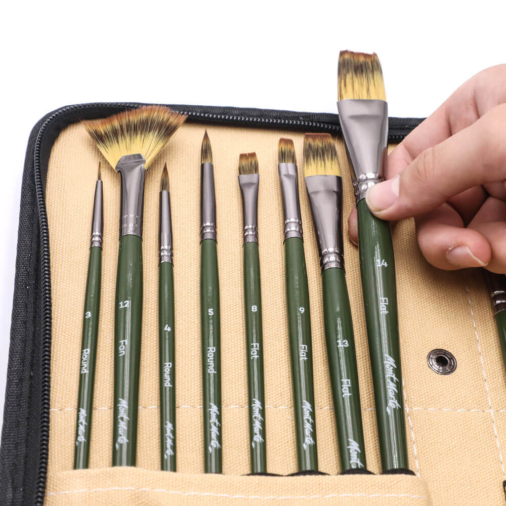 Hand picking up a taklon paint brush from a Mont Marte brush wallet, each of a different size with a green handle.