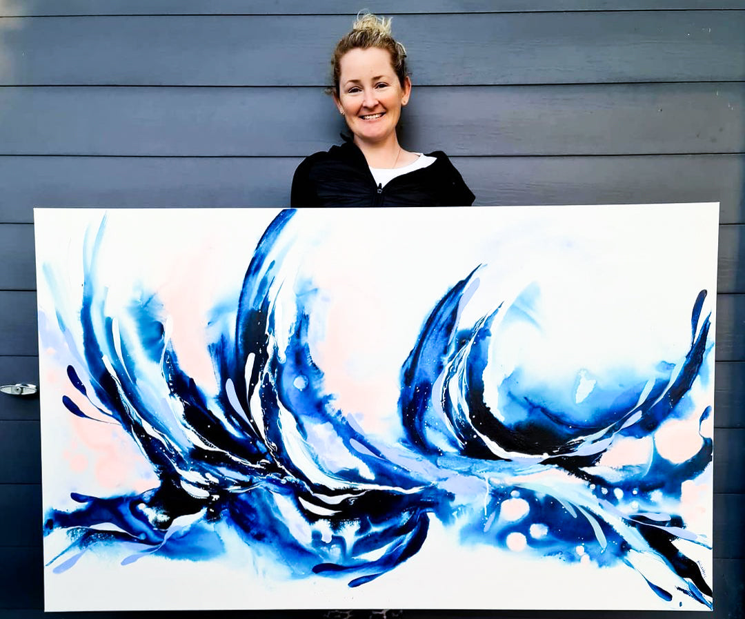 Megan Walters holding a large white canvas with blue abstract pour painting on it.