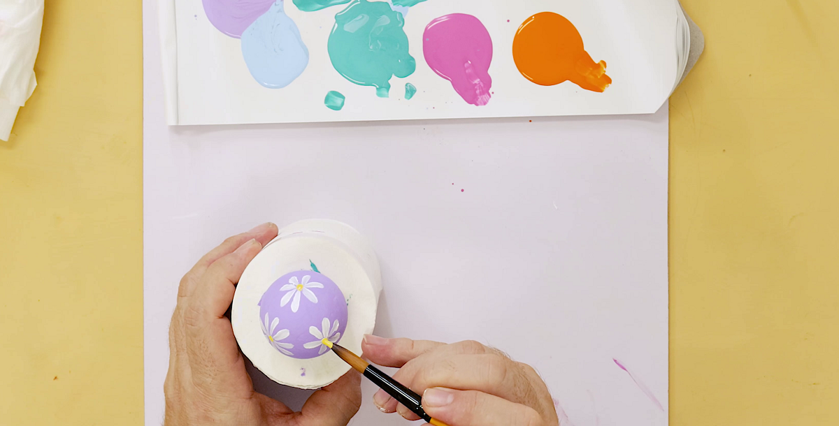Hand painting daisies on a purple Easter egg.
