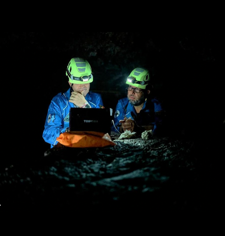 Two scientists looking at a computer screen in a dark cave