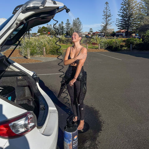 Female surfer washing after a surf in carparl
