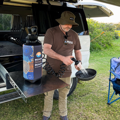 Man washing a pan while camping using a Beach Shower