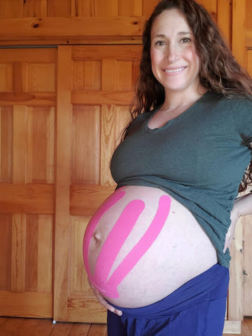 pregnant woman smiling with baby belly supported by pink pregnancy tape