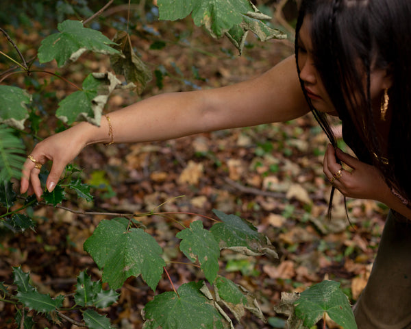 a girl's hand touching a plant in a forest