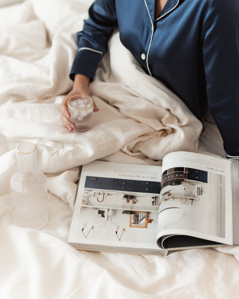 woman holding water and reading magazine on the bed