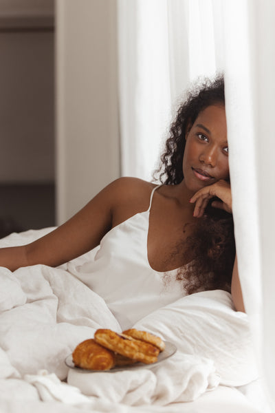 woman in silk and a plate of croissant on the bed