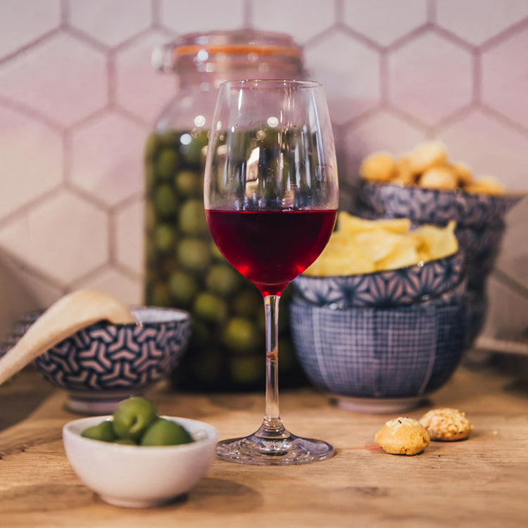 A glass of red wine on a wooden countertop with an assortment of food around