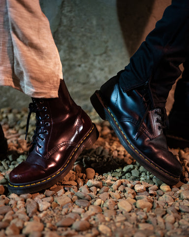 two sets of feet wearing doc martens with pants on a gravel surface