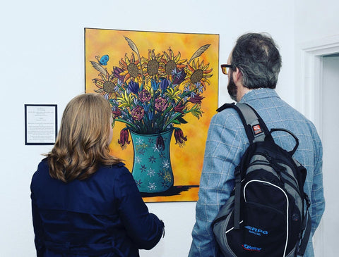 A husband and wife viewing a painting of some flowers  