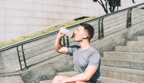 Man sitting outside on cement steps drinking from a water bottle