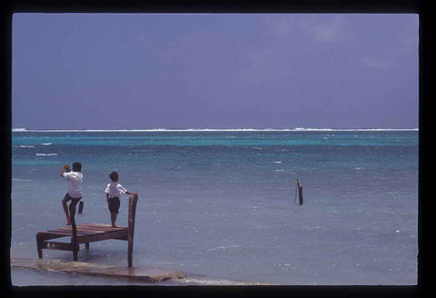 Belezian school kids dangle on a dock after school. They peer out overlooking the crystal blue ocean. 