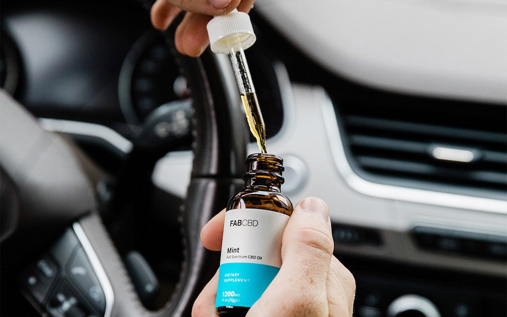 Someone takes the dropper out of a CBD bottle while sitting in the car