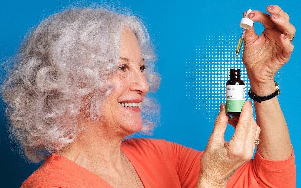 A woman holds up a bottle of CBD oil and takes the dropper out.