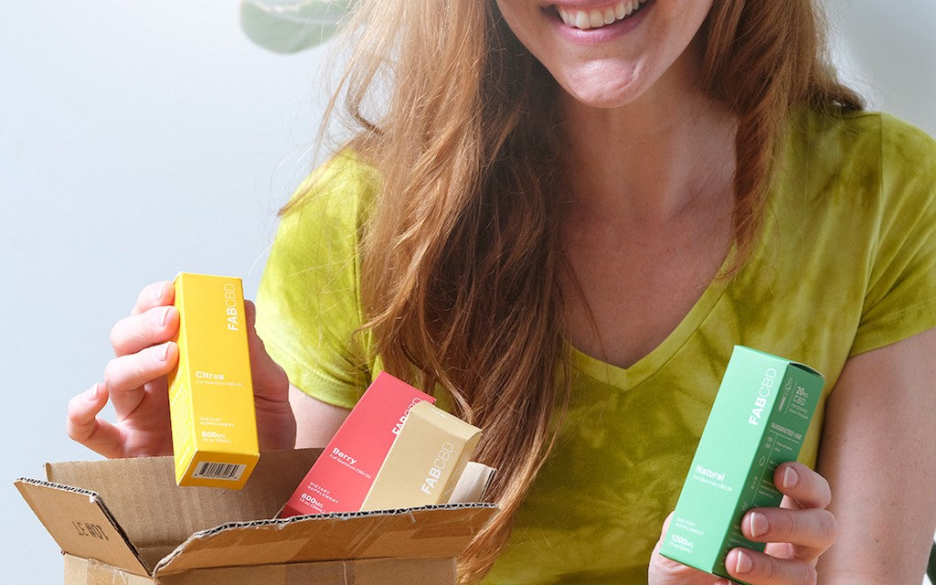 A young woman smiles brightly as she opens her shipment of CBD oil