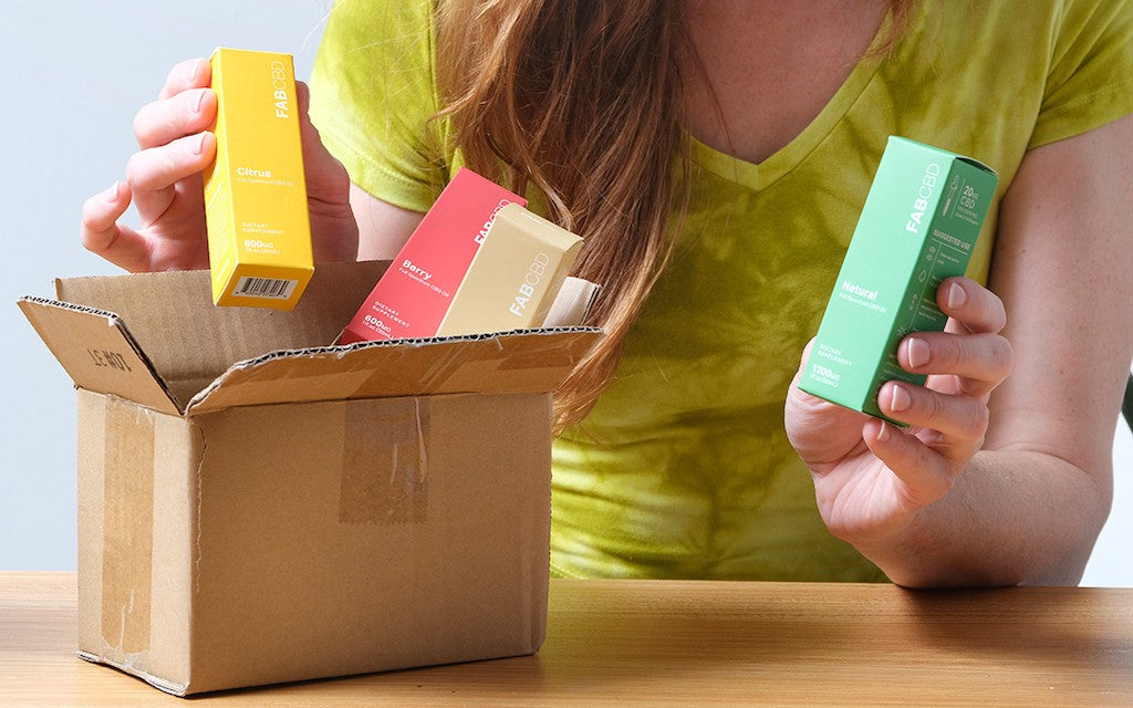 A woman opens up a box from the mail containing multiple CBD oils.