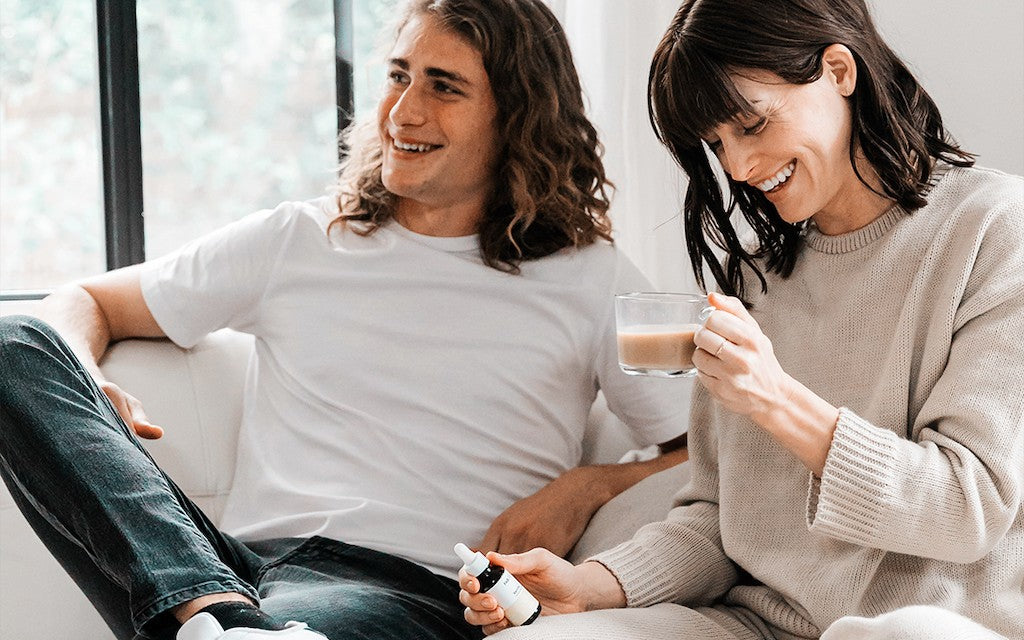 A young woman and man sit together on a white couch smiling and laughing