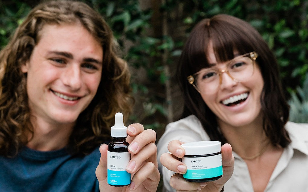 A young man and a young woman smile and show their CBD products to the camera