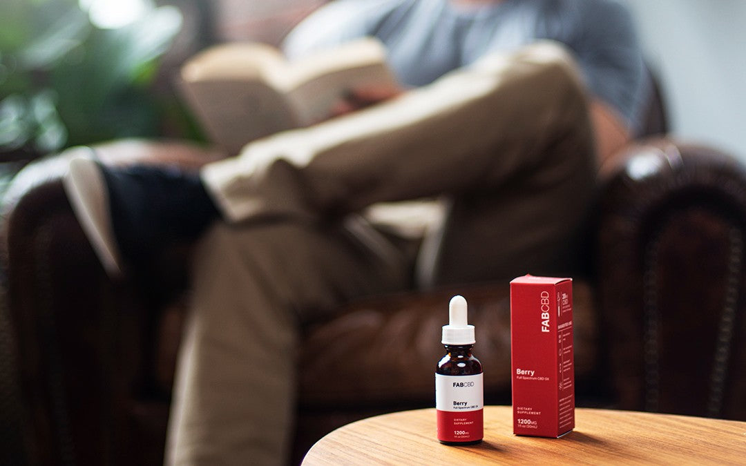 A Man Reading a Book While His Bottle of Berry Flavored FAB CBD Full-Spectrum CBD Oil Sits on a Table