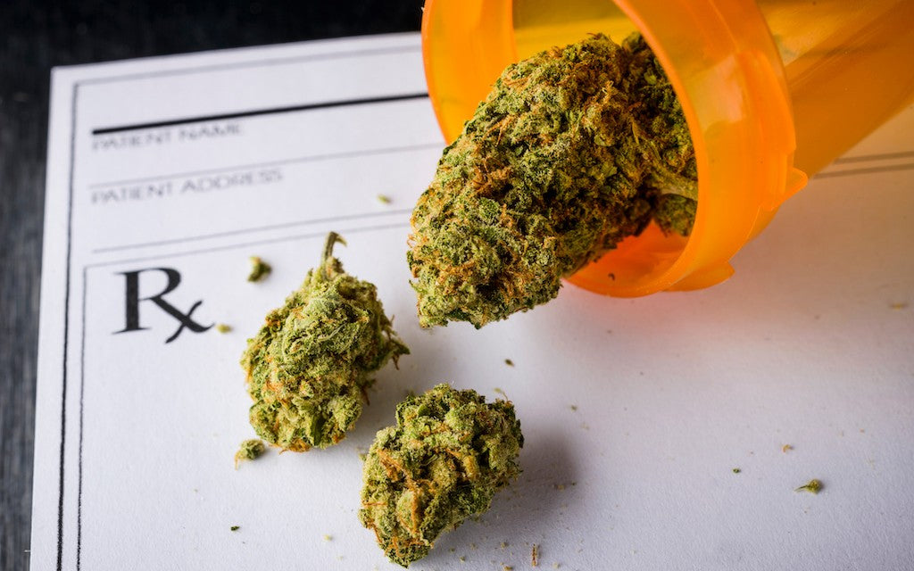 Cannabis buds tumble out of an orange prescription bottle onto a doctor's prescription pad.