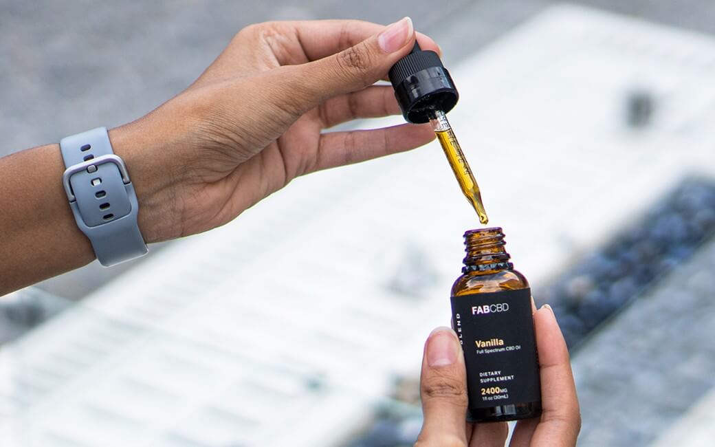 A young woman holds a bottle and dropper of CBD oil