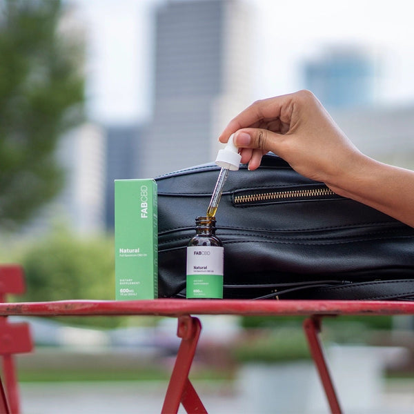 Someone taking the dropper out of a bottle of CBD next to a backpack on a park bench