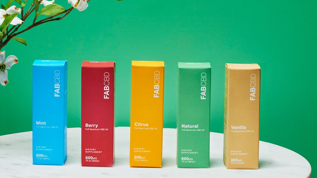 Colorful boxes of FAB CBD oils lined up next to each other on a green backdrop